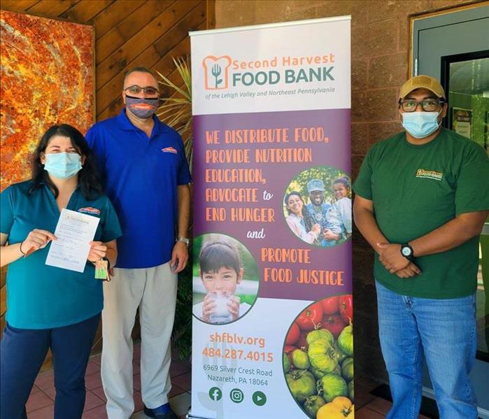 Three people stand with food bank sign