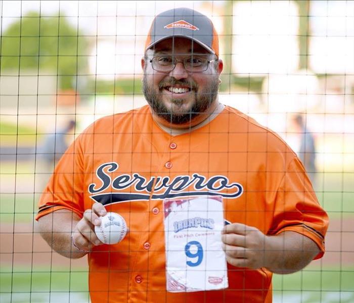 Man with glasses in orange jersey and hat holding baseball and paper