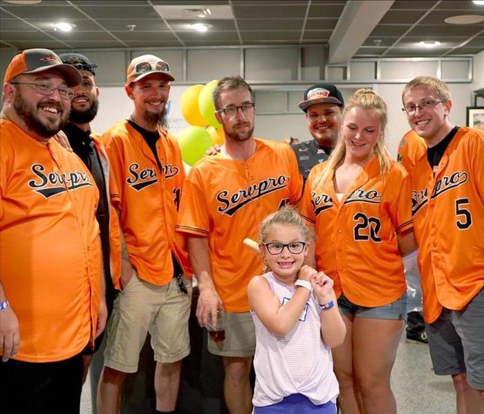 little girl with bat surrounded by employees in jerseys
