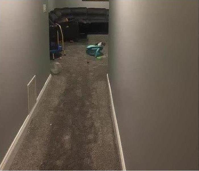 Hallway of a basement at the end of a hallway there is a black couch, wet carpet