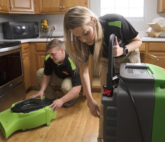 Two SERVPRO technicians in a kitchen setting up equipment.